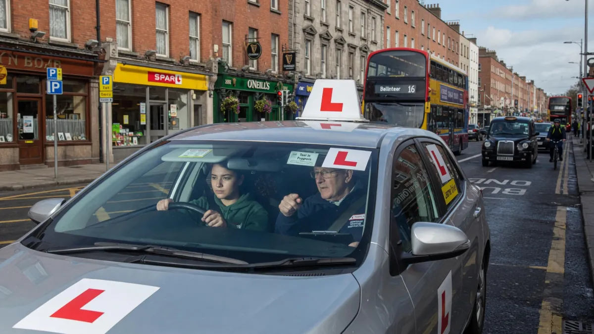 A learner driver with L-plates taking a driving lesson with an instructor on a busy Dublin city street